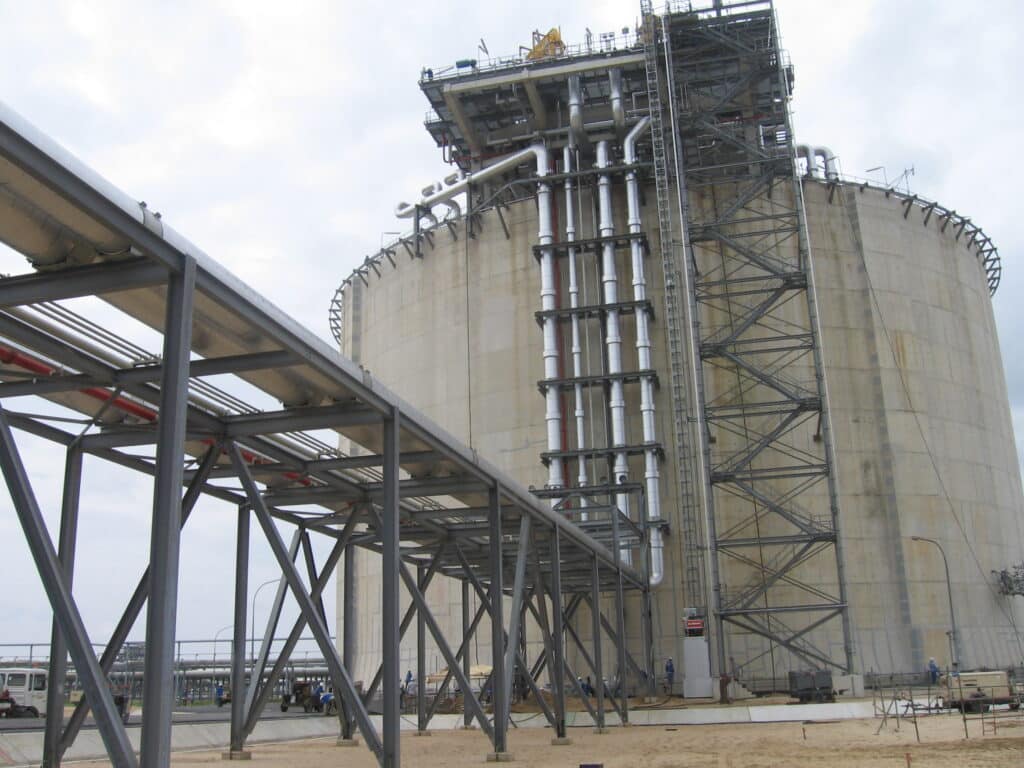 Réservoir industriel cylindrique en béton avec une structure métallique externe, des tuyauteries verticales et une passerelle surélevée au premier plan.